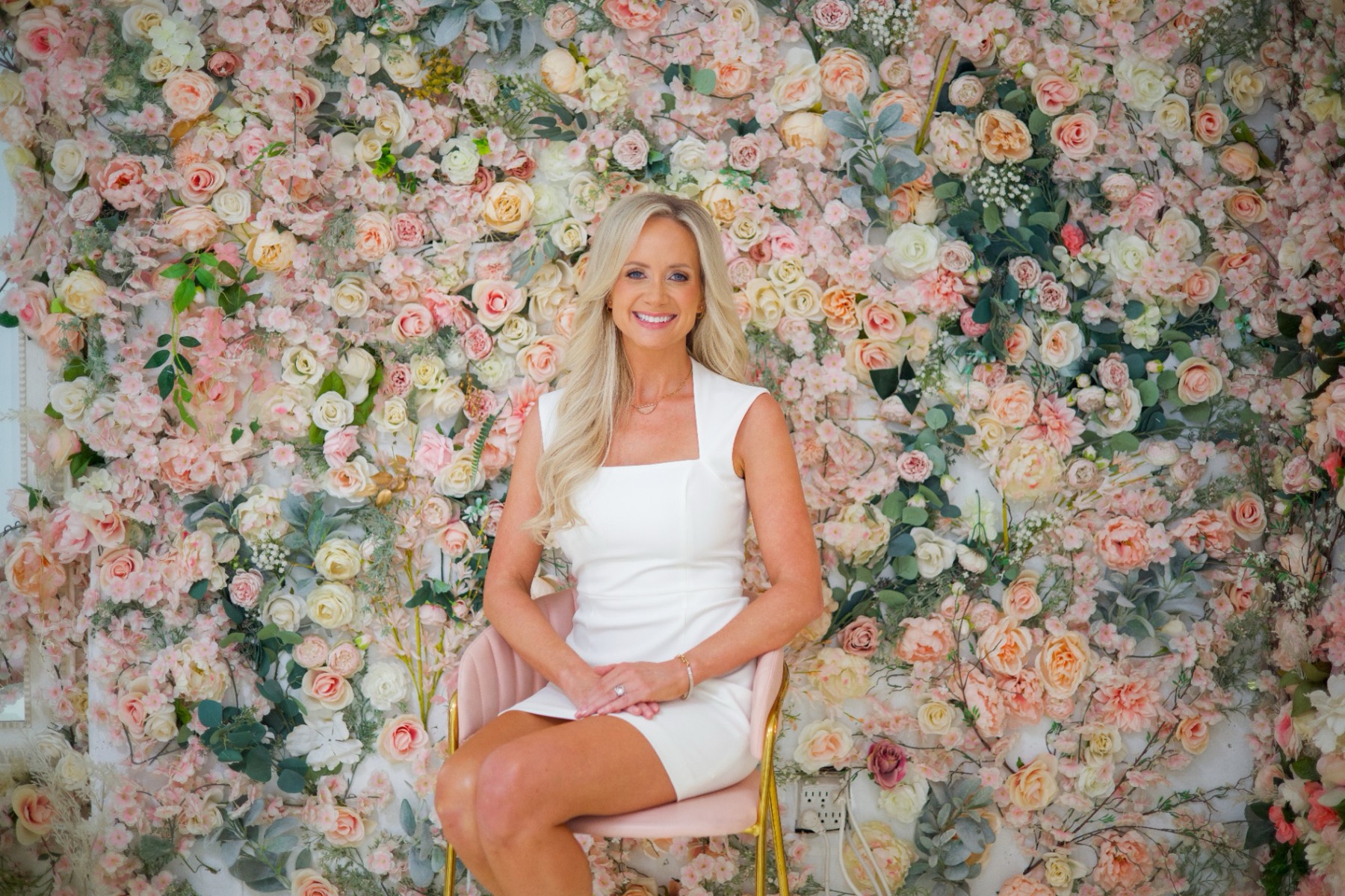 Brittany Stanley in a white dress seated in front of a floral wall